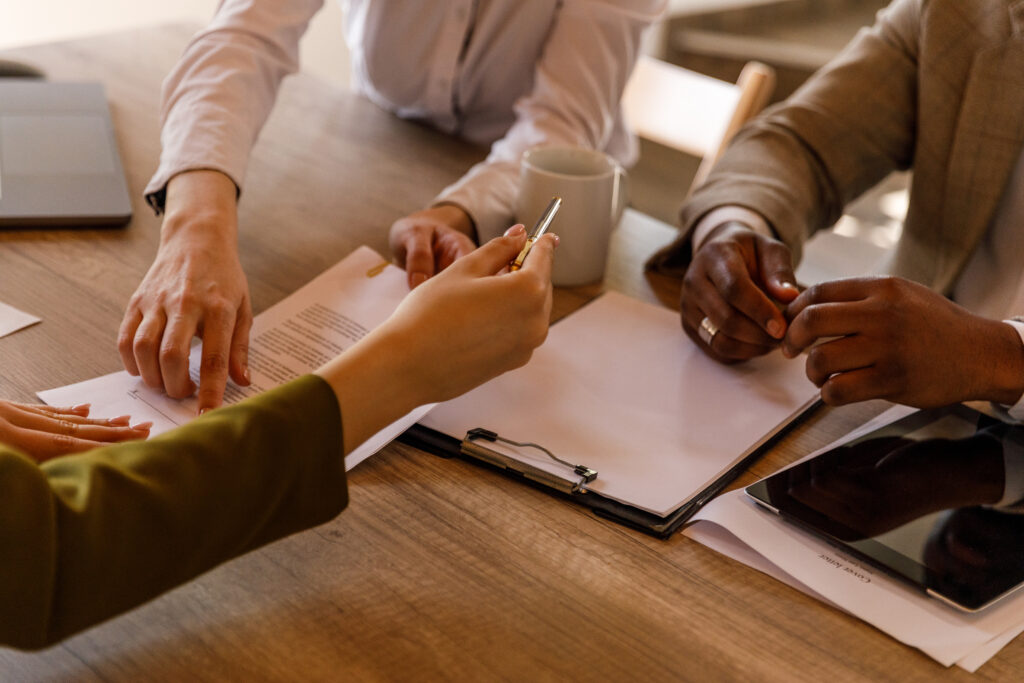 Photo of a desk with a clipboard and three people's hands.