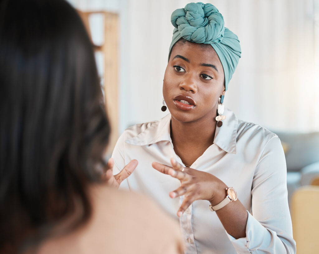 Photo of a woman in a blue headscarf talking to a witness with dark brown hair.